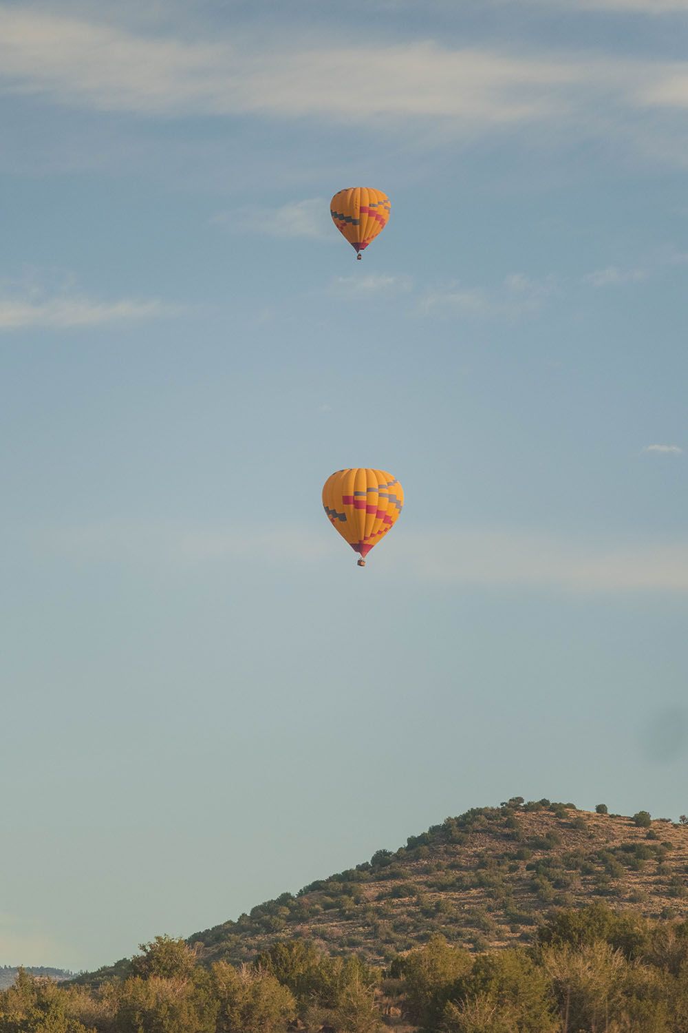 Two hot air balloons flying over a mountain in a blue sky