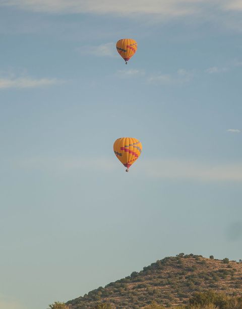 Two hot air balloons flying over a mountain in a blue sky