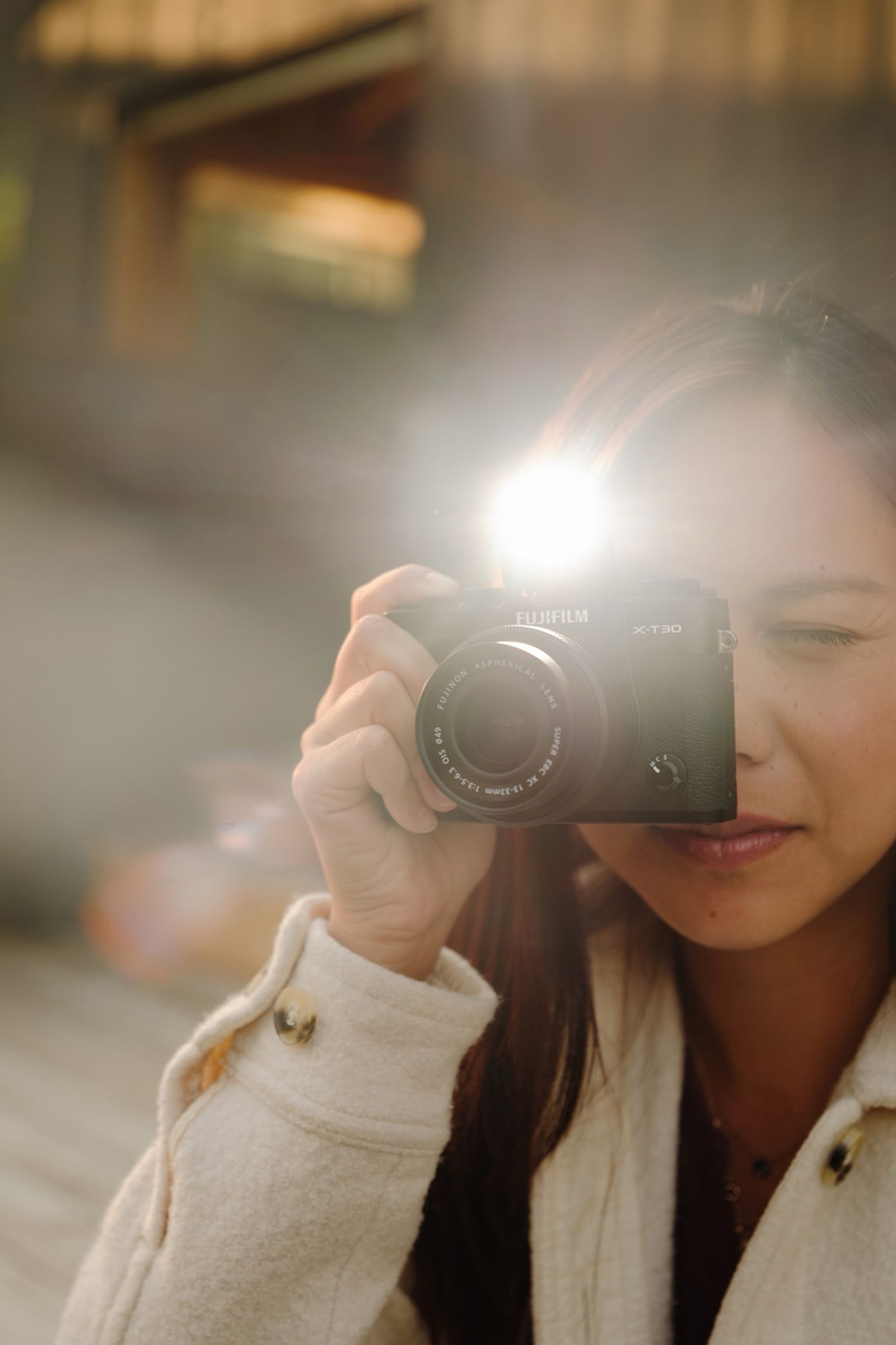 A person wearing a white coat makes a photo with FUJIFILM X-T30 III, flash brightening the scene, creating a soft, blurred background effect