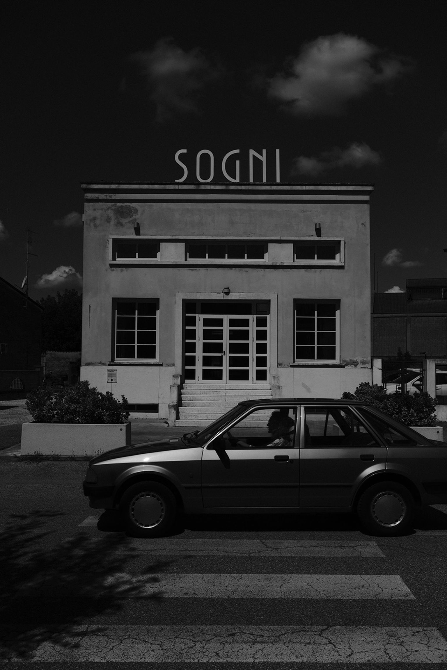 A vintage car parked in front of a building in a dramatic scene with clouds in the sky
