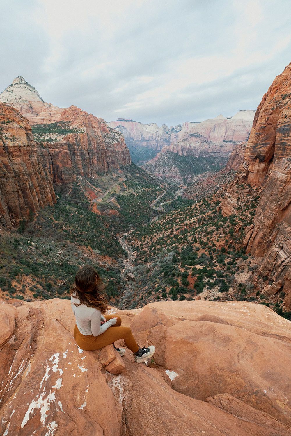 A woman sitting on the edge of a rock overlooking a ravine
