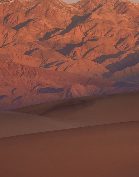 A sandy desert in shadow with jagged orange mountains in the background