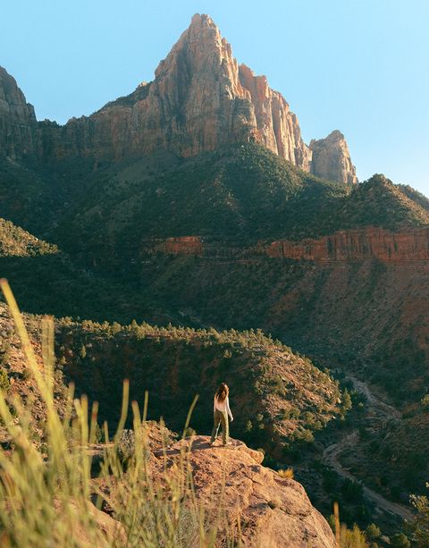 A woman standing on the edge of a cliff, looking a tall mountain in the distance