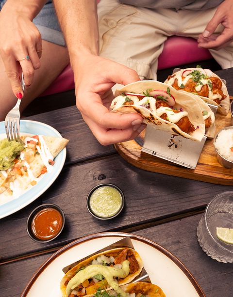 People enjoying tacos with toppings, nachos, and sauces on a wooden table, sharing a relaxed dining experience