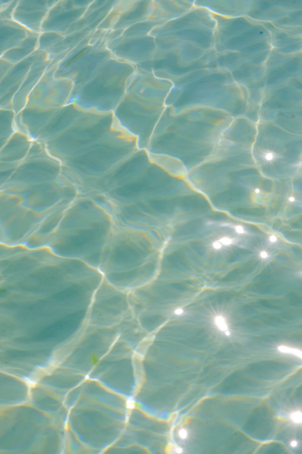 Sunlight sparkles on clear turquoise water, creating a wavy, textured surface pattern