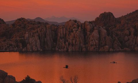 Birds in silhouette flying over a lake with mountains in the background at sunset
