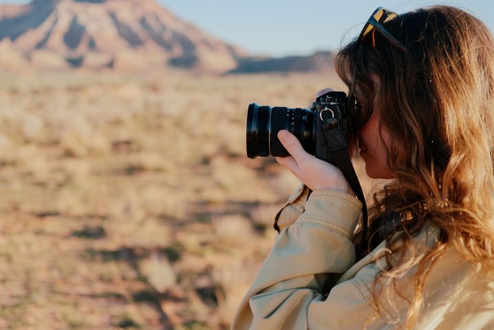 Side profile of a woman holding a Fujfilm camera to her eye with a blurred desert landscape in the background