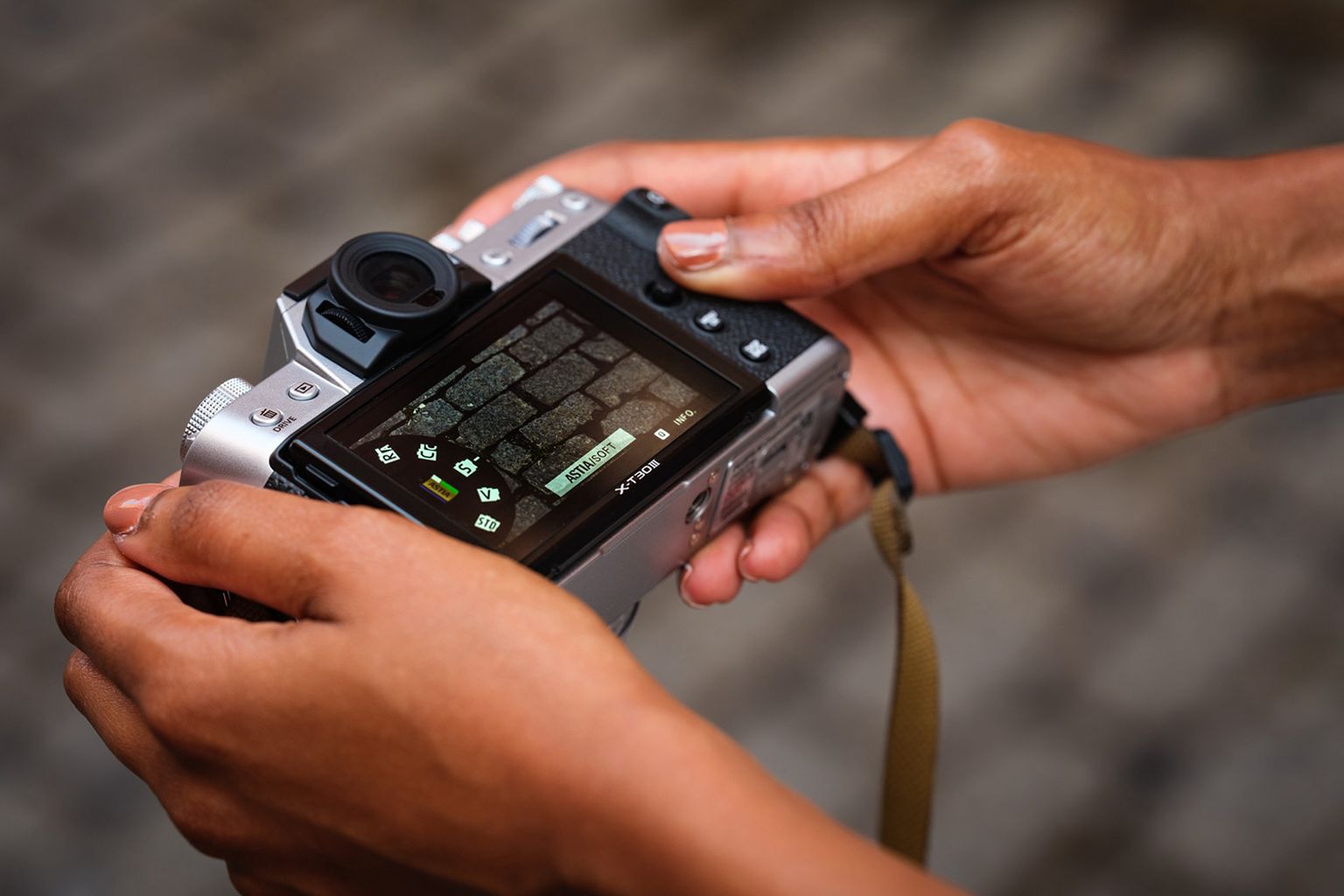 Hands holding a digital camera with its screen displaying a brick wall in focus, buttons visible on the side