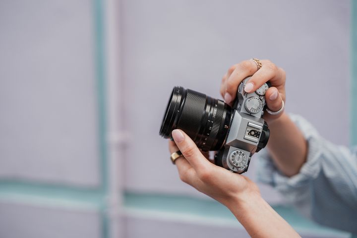Hands adjusting a vintage-style camera, focusing on the dials and lens, against a soft purple background
