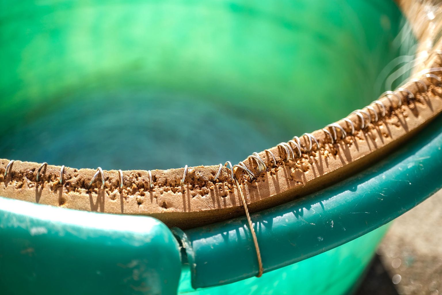 Close-up of a green plastic bucket with a worn, rope-bound rim, highlighting sunlit textures and fine details