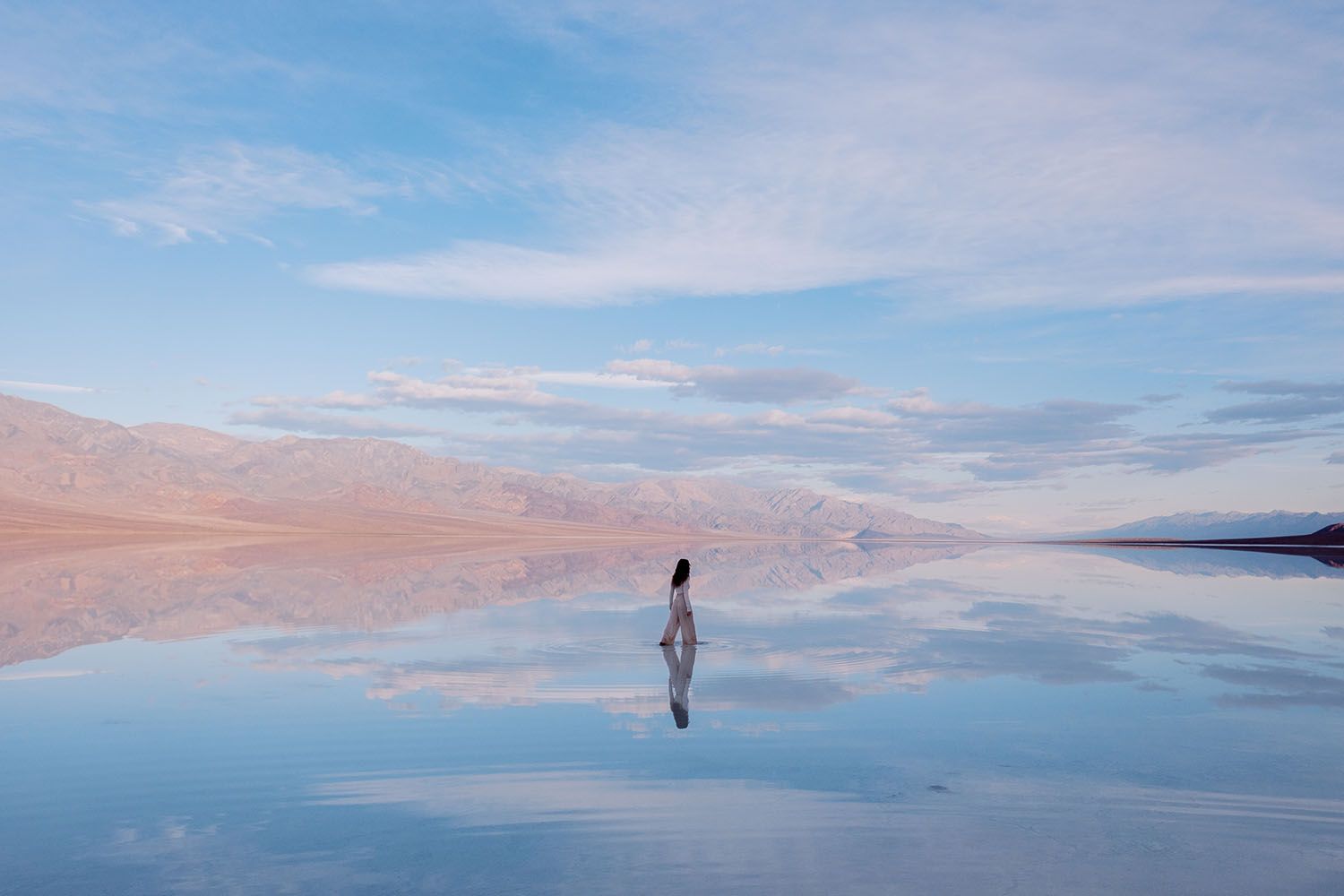 A person walking across a watery surface reflecting the sky