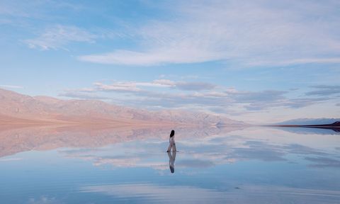 A person walking across a watery surface reflecting the sky