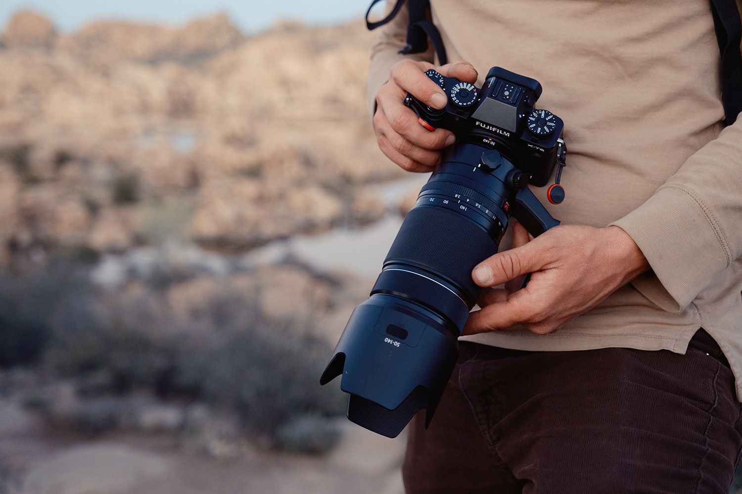 Person holding a professional camera with a long lens, standing in a rocky outdoor landscape