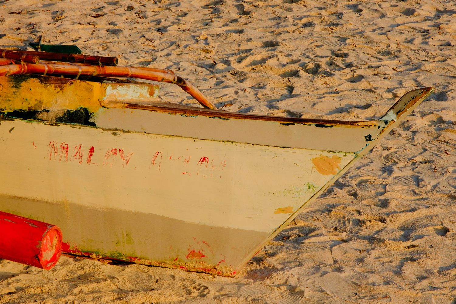 A close-up of a weathered wooden boat on sandy shore, with visible peeling paint and worn textures in soft, warm light