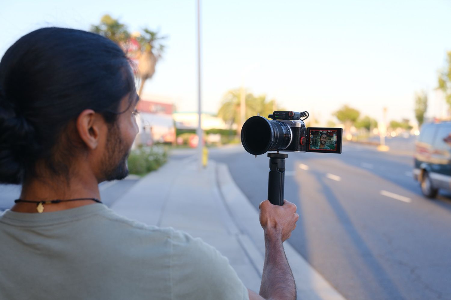 A person films themself using a camera with a flip-out screen on a handheld stabilizer