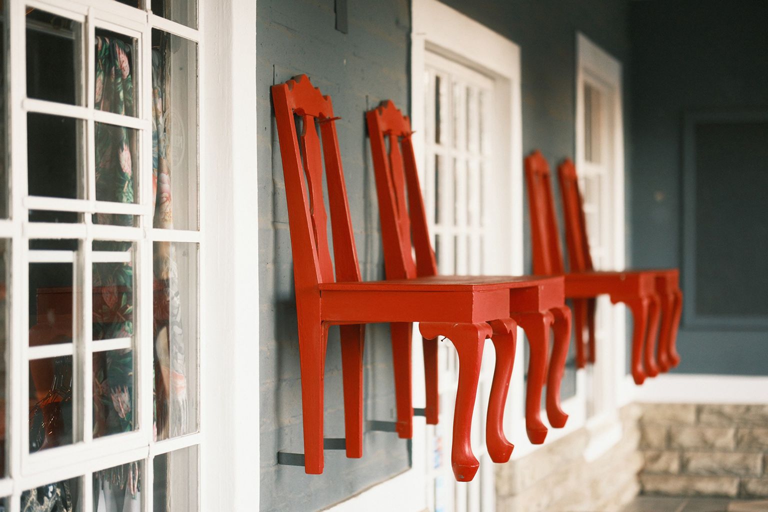 Red chairs mounted on a wall, with a window and blue-grey wall in the background