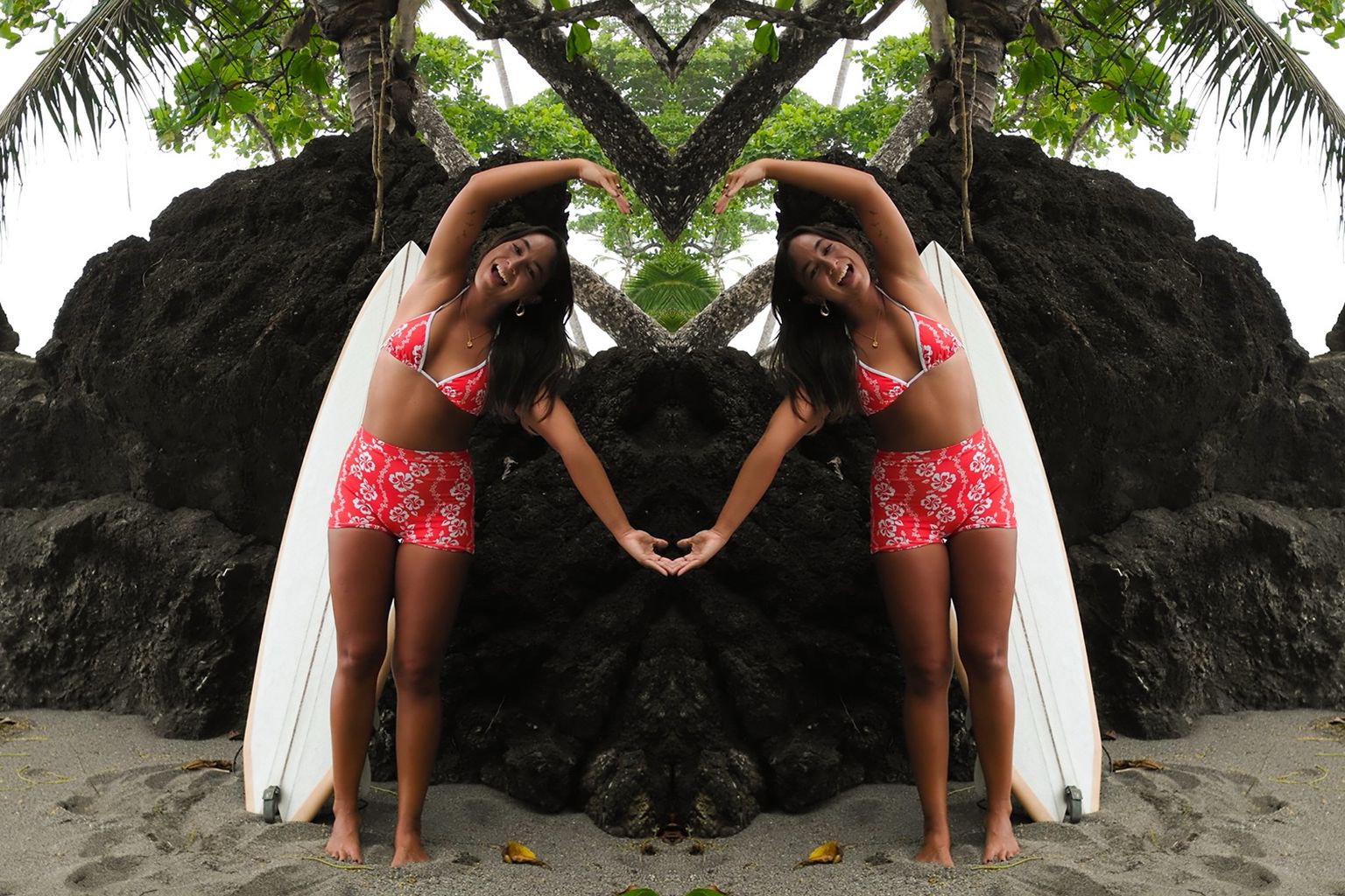 Woman in red swimsuit posing with a surfboard on a beach, mirrored image effect, surrounded by rocks and greenery