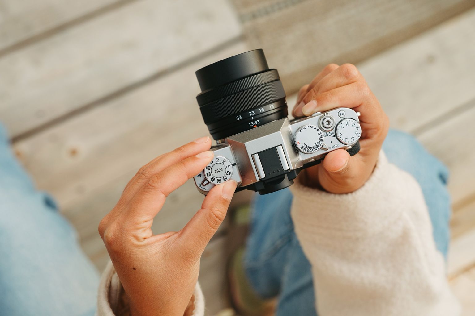 Hands holding a vintage-style camera, viewed from above, with wooden floor in the background