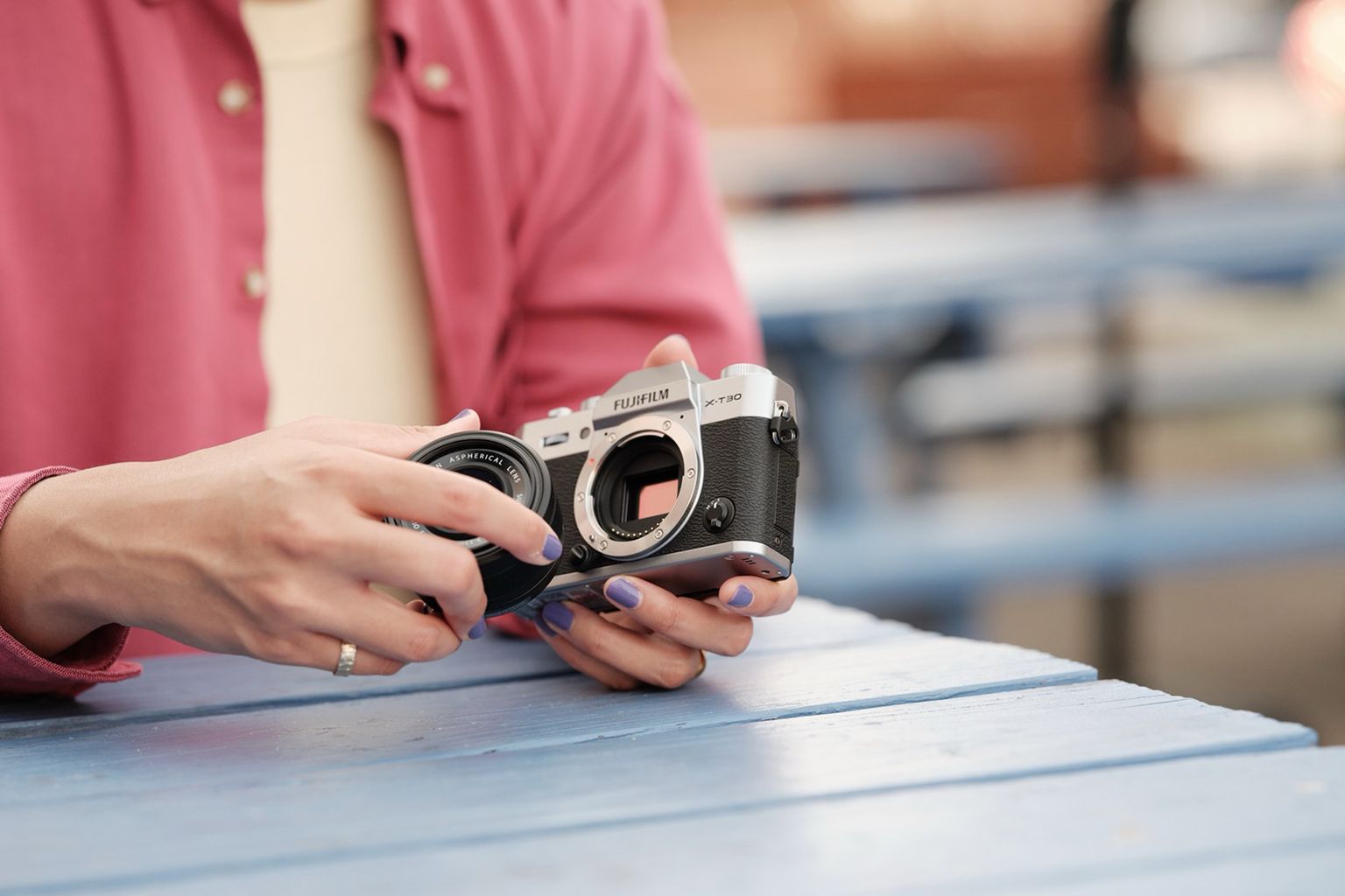 Person holding a vintage camera at a blue picnic table, changing the lens