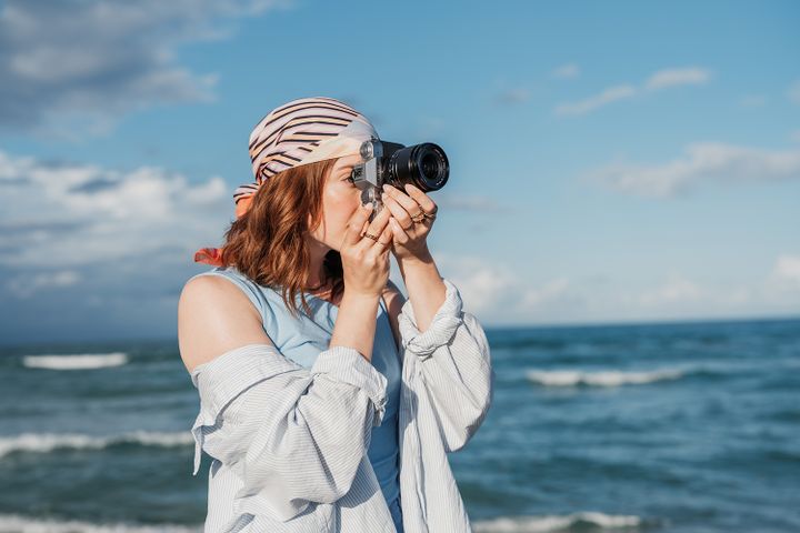 Woman with a headscarf making a photo with a camera by the ocean on a sunny day