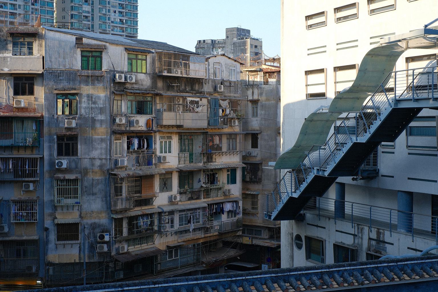 Old apartment buildings with air conditioners, a weathered exterior, and external stairways under clear blue sky