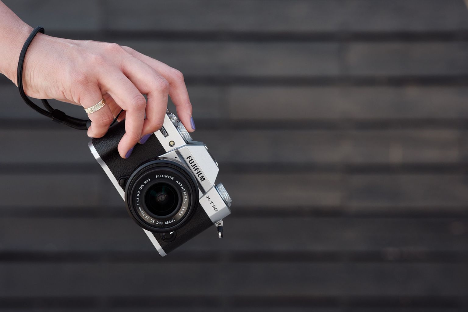 A hand holding a Fujifilm camera with a wooden textured background
