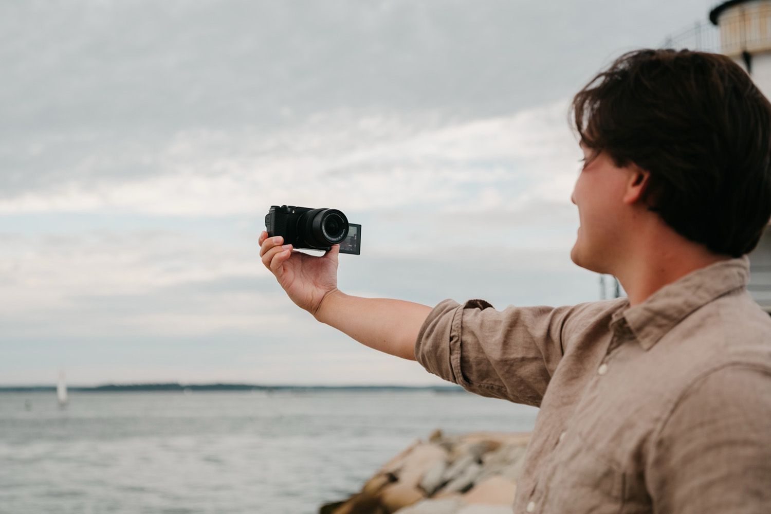 Person making a selfie with a camera by the seaside, facing the ocean under a cloudy sky
