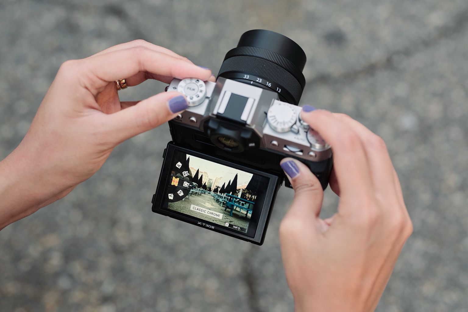 Hands holding a digital camera with a flip screen displaying an outdoor scene and settings