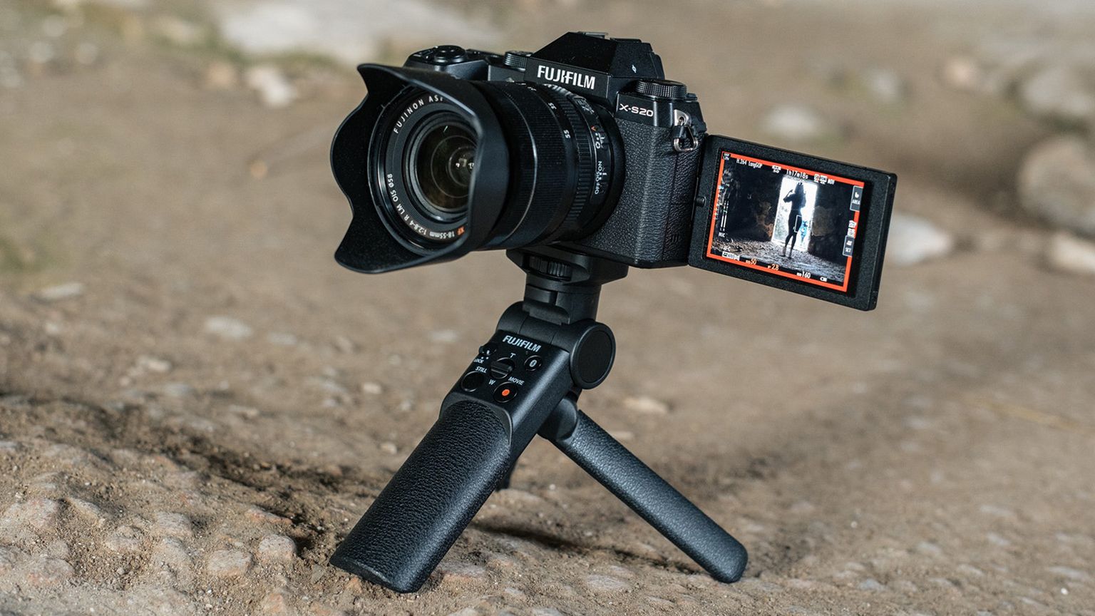 Fujifilm camera on a tripod with an articulating screen displaying a black-and-white image, set on a rocky surface