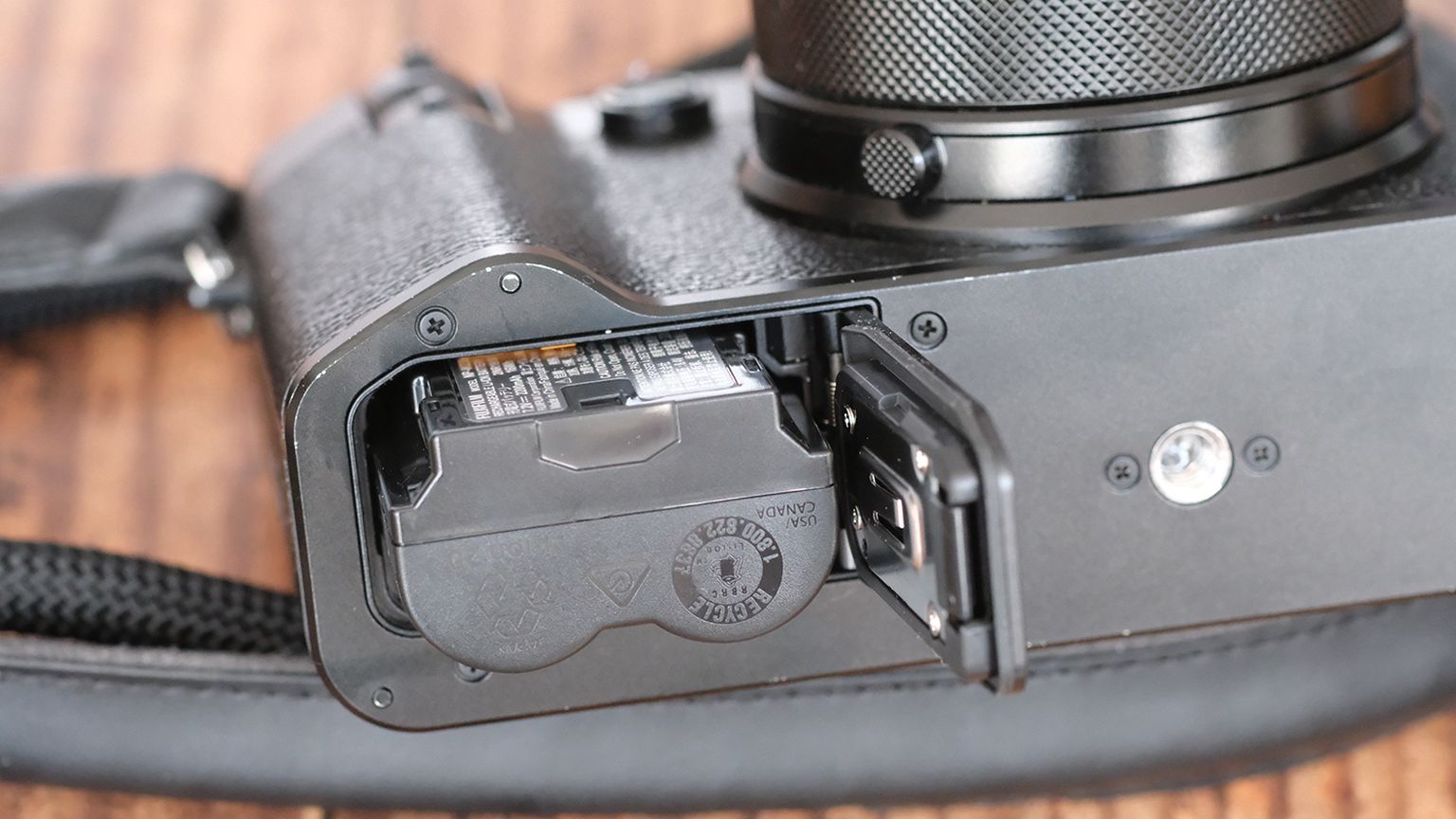 The underside of a camera showing an open battery compartment with the battery partially inserted