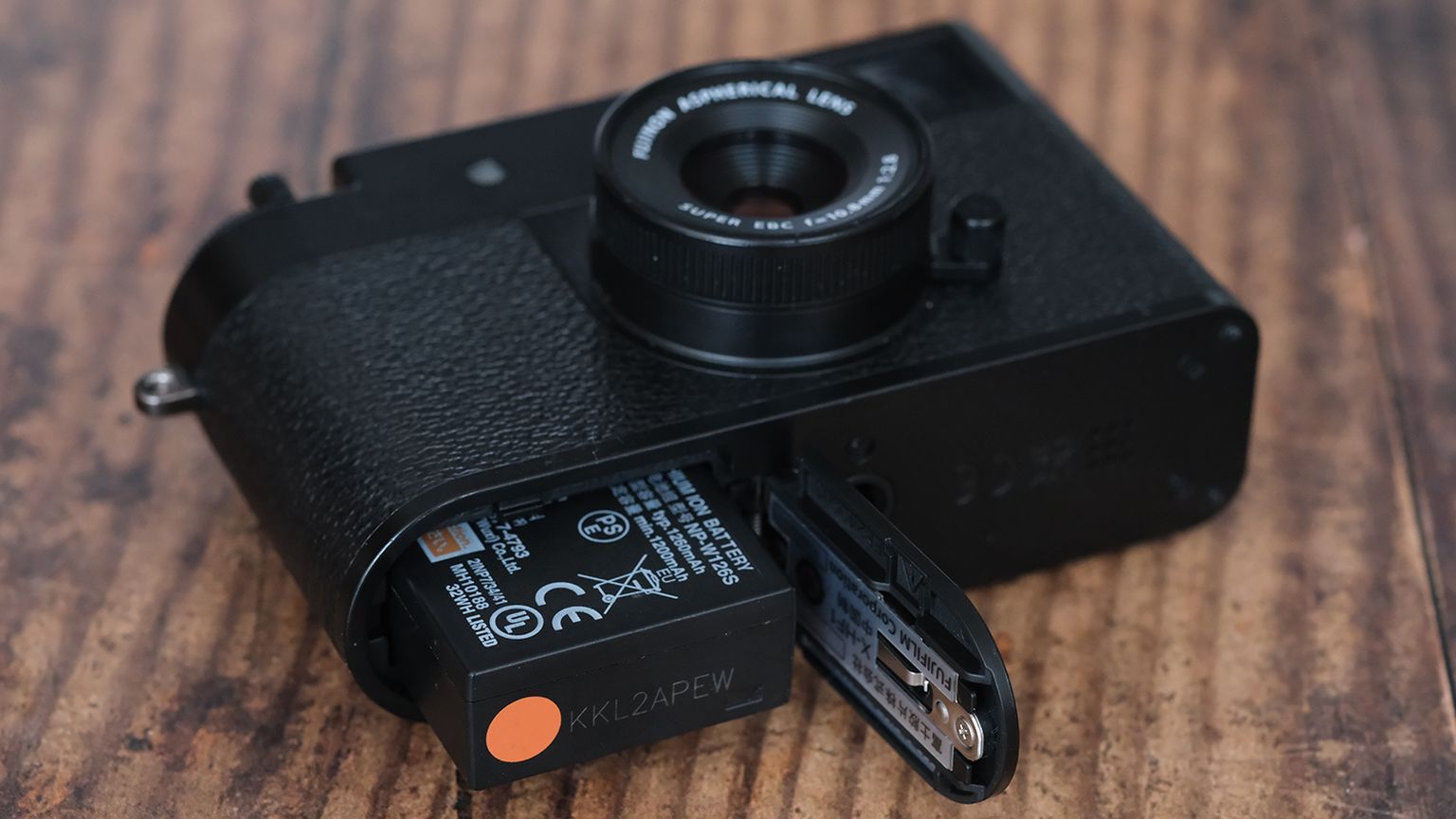 A black camera on a wooden surface with its battery compartment open