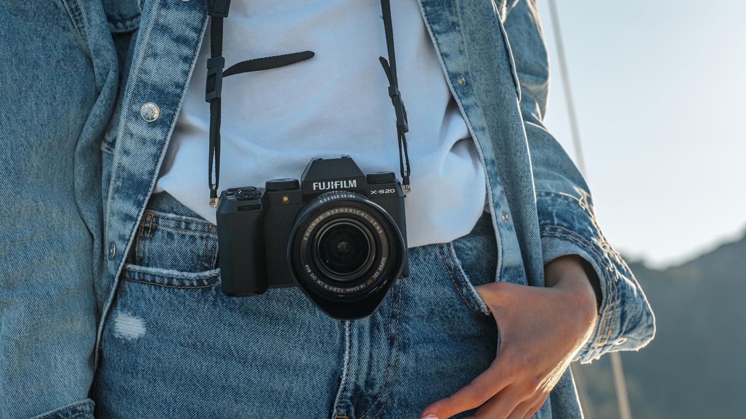 Person wearing a denim jacket and jeans, with a Fujifilm camera hanging from their neck