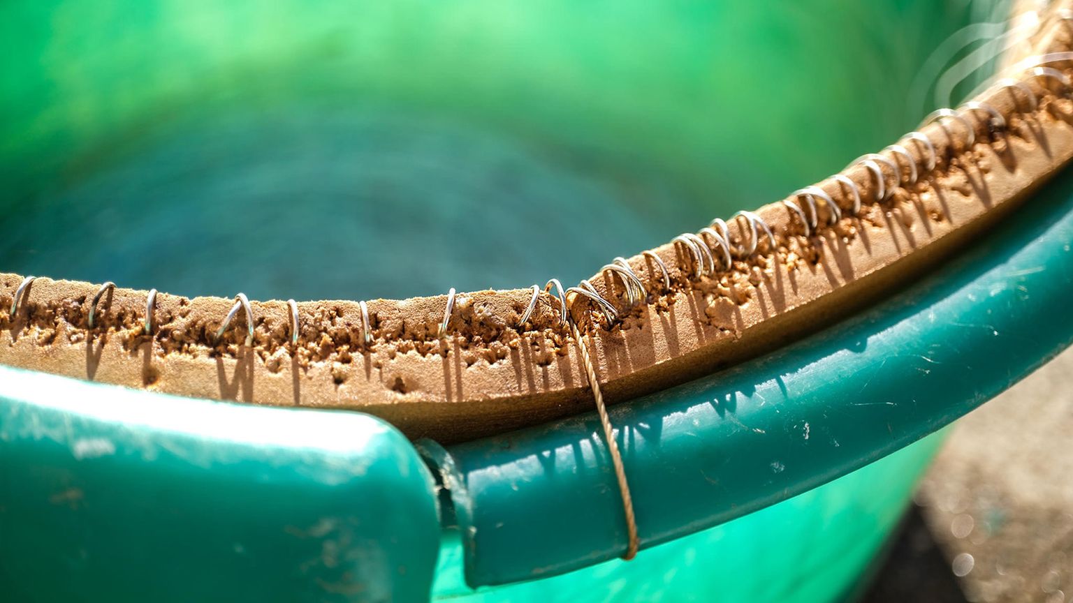 Close-up of a green plastic bucket with a cork and wire handle, showing wear and texture from use, in bright sunlight