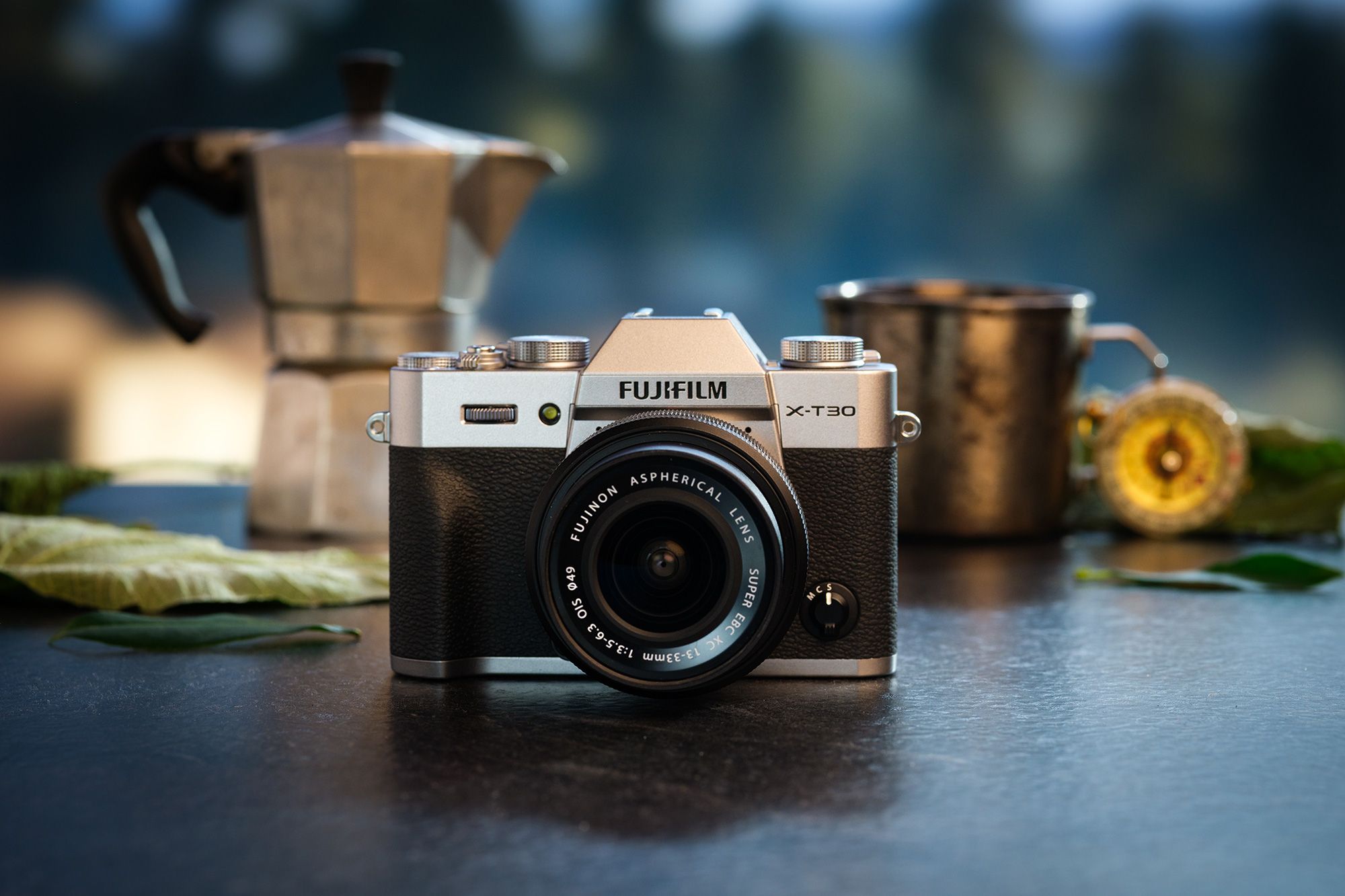 FUJIFILM X-T30 III on a table with a moka pot, a metal cup, and leaves in the background.