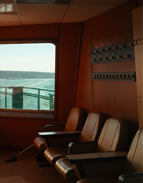 Empty seats in a ferry cabin with a view of the ocean through a window. Pegs on the wall and a broom on the floor.