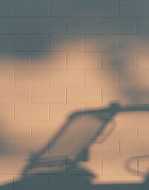 Shadow of a shopping cart cast on a beige brick wall, creating an abstract pattern with soft lighting.