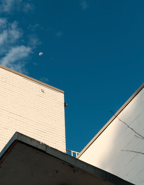A white brick building against a clear blue sky, with the moon visible above and a few clouds in the corner.