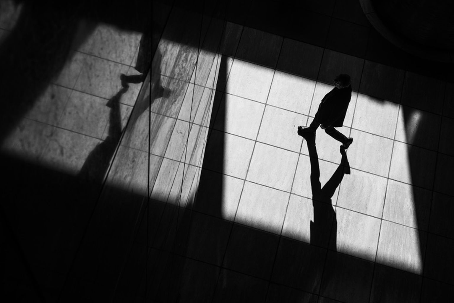 Silhouetted person walking across a sunlit tiled floor, casting a long shadow, with dramatic light and geometric patterns. Silhouetted person walking across a sunlit tiled floor, casting a long shadow, with dramatic light and geometric patterns.