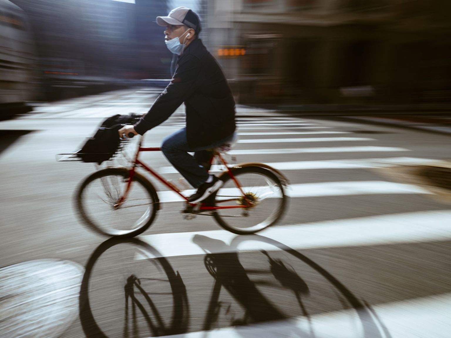 Person wearing a mask rides a red bicycle across a city street, motion blur effect highlighting speed and movement. Person wearing a mask rides a red bicycle across a city street, motion blur effect highlighting speed and movement.